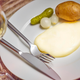 Plate of Swiss raclette with cornichon, potato, and pearl onions beside glass of white wine